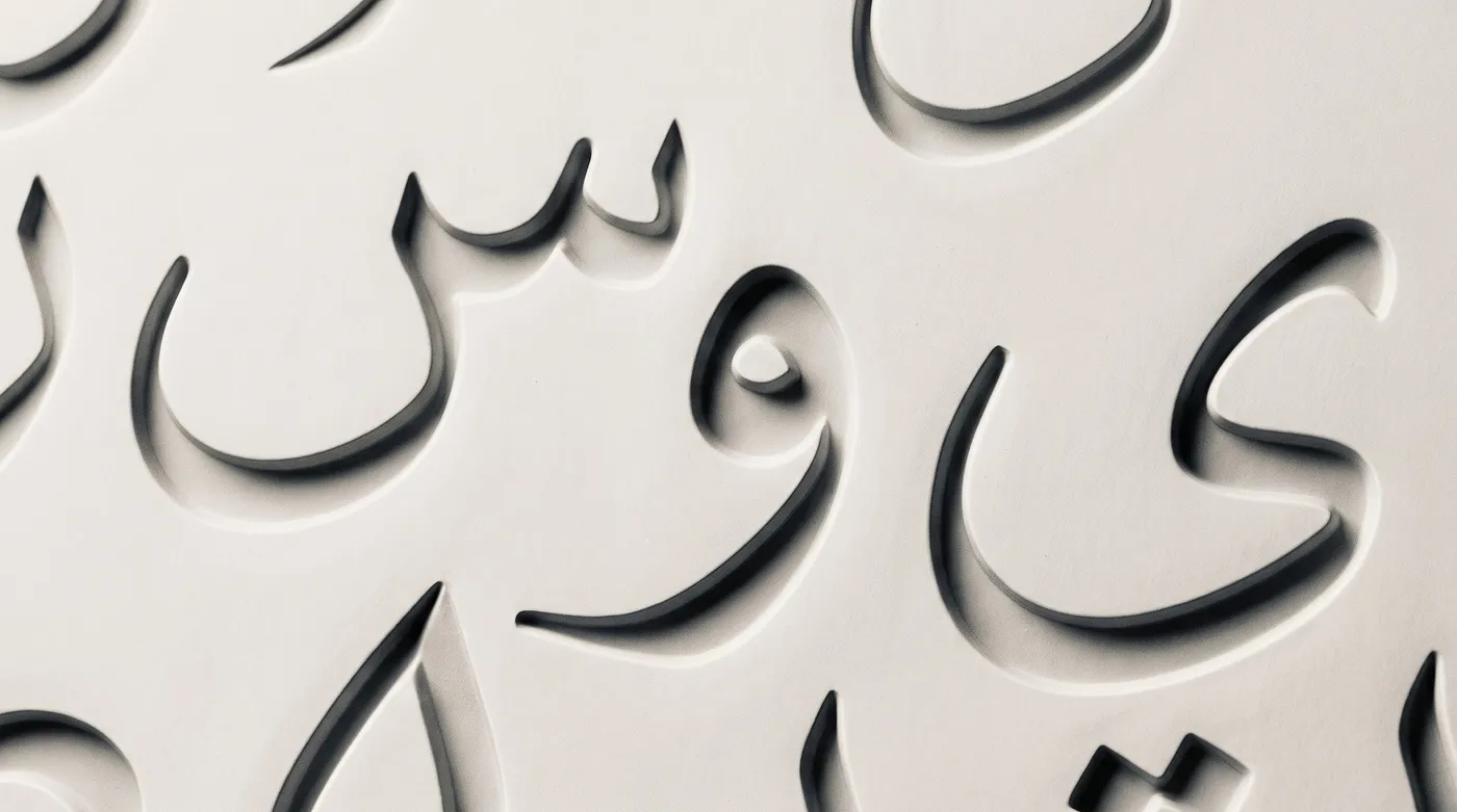 Arabic letterforms embossed in low relief on a pale surface, cropped so the letters read as abstract shapes.